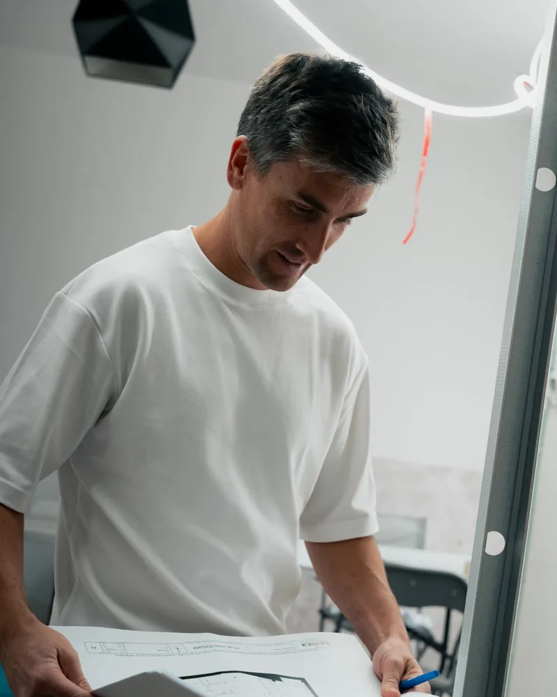 Matthieu Burin, t-shirt blanc, tenant un plan architectural dans un local en travaux
